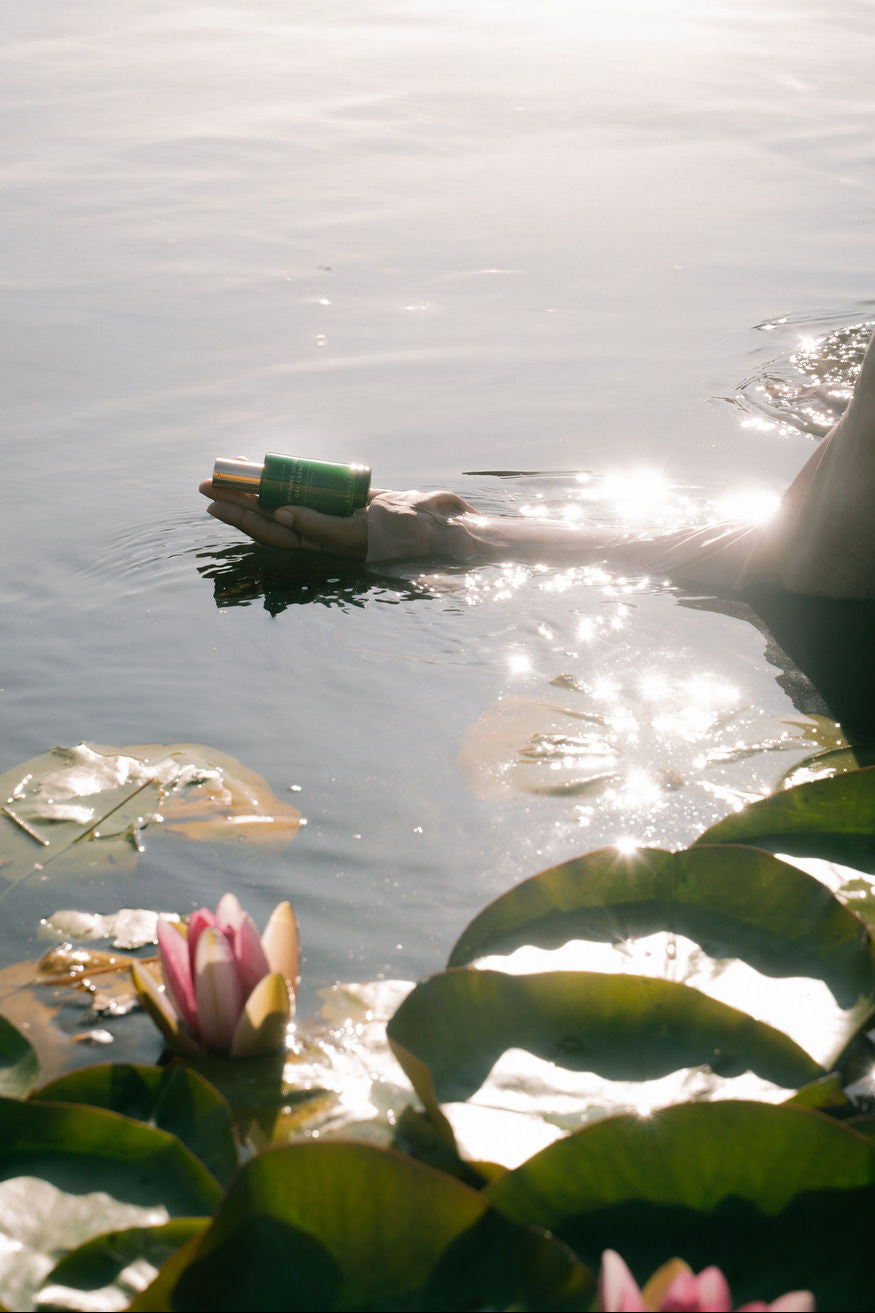 Person swimming with a green bottle in a body of water surrounded by lily pads.